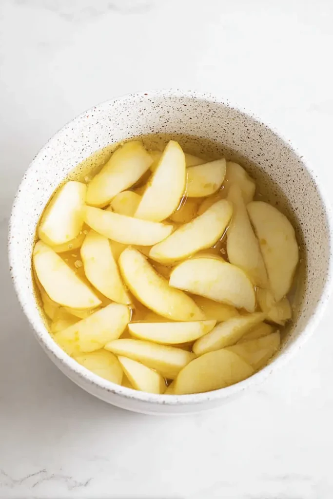 Macerated apple slices for Easy Cinnamon Apple Cake in ceramic bowl