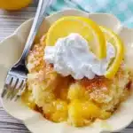 Plated magic lemon cobbler with golden crust, whipped cream, and lemon slices