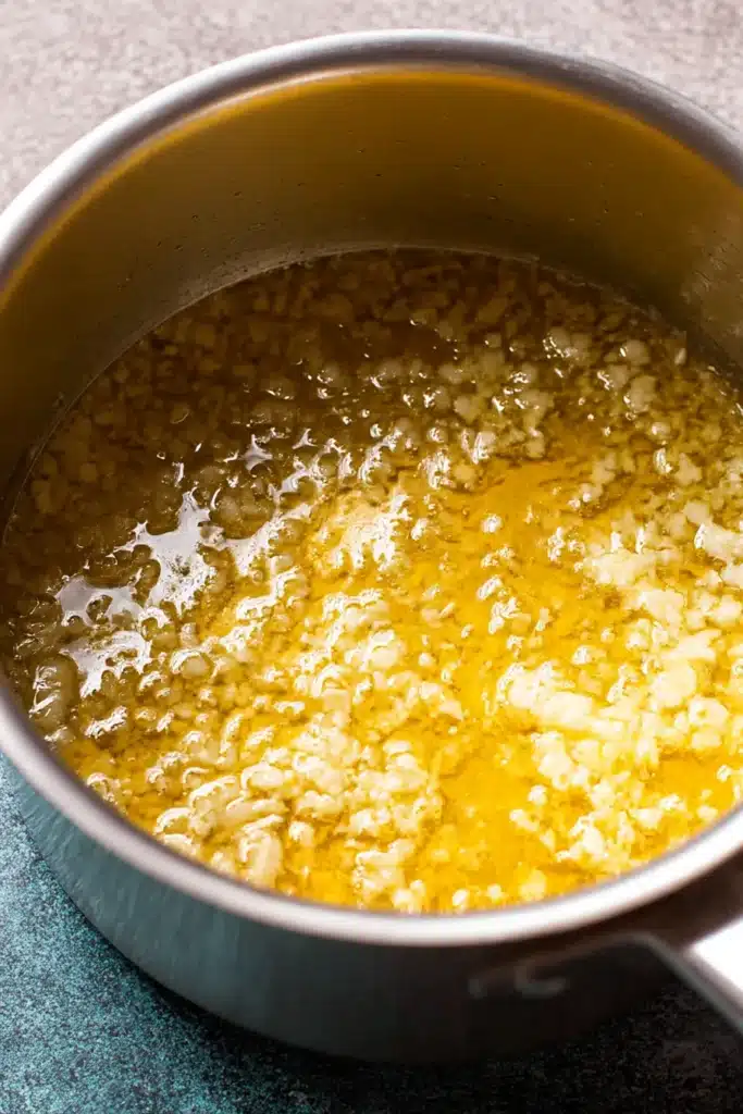 Close-up of sautéed garlic in melted butter inside a stainless steel saucepan