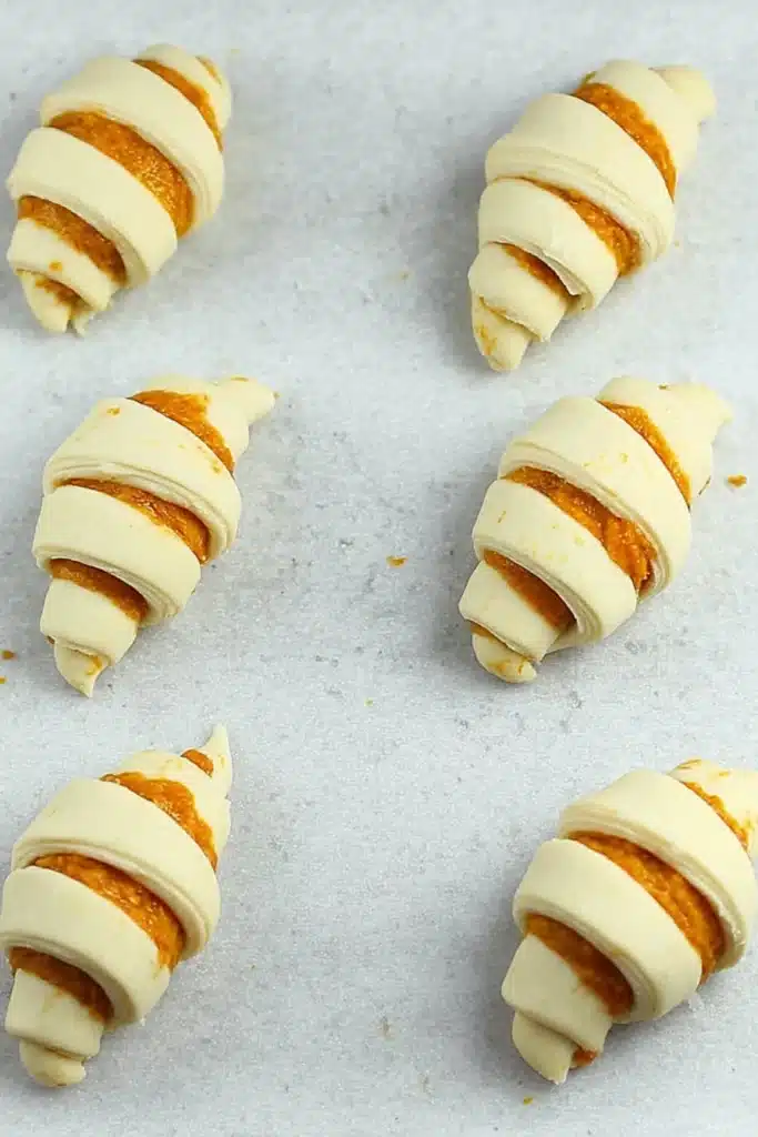 Unbaked mini pumpkin pie crescent rolls on parchment paper