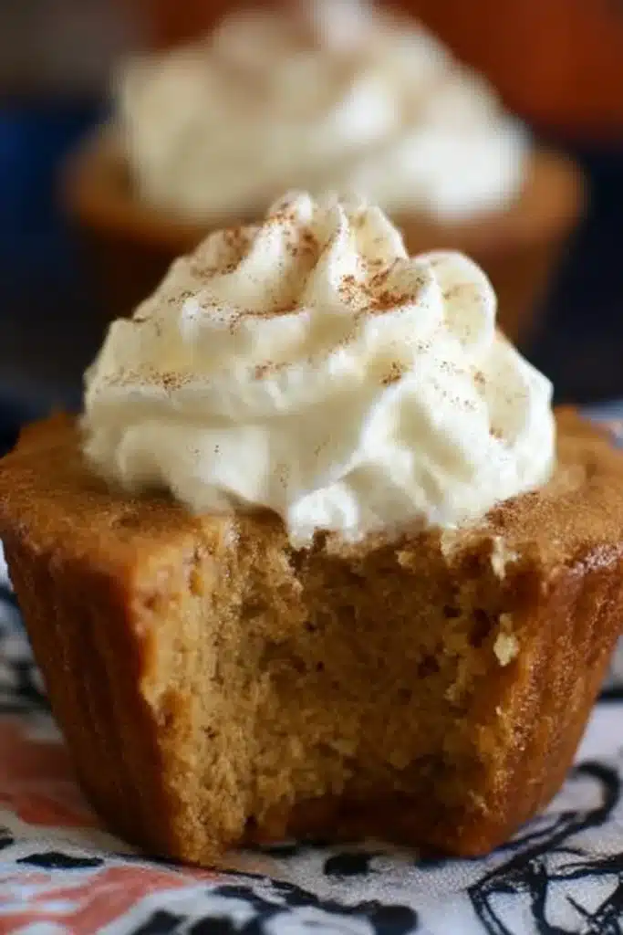 Easy Pumpkin Pie Cupcakes topped with whipped cream and cinnamon, with a moist custard-like center and a visible bite