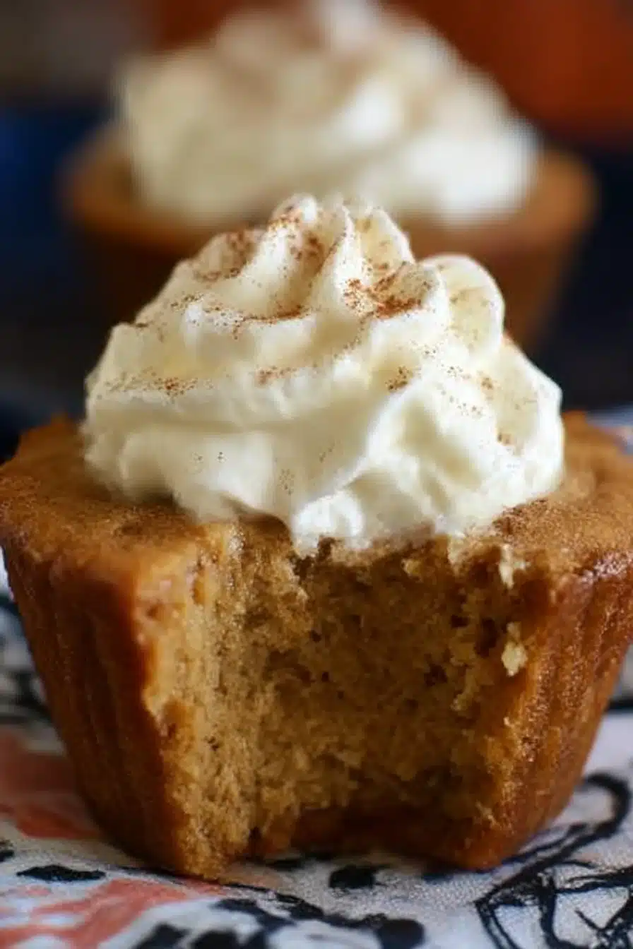 Easy Pumpkin Pie Cupcakes topped with whipped cream and cinnamon, with a moist custard-like center and a visible bite