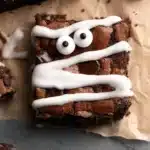 Gluten-free Halloween mummy brownies with white icing and candy eyes on parchment