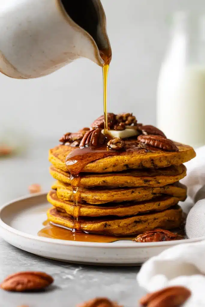 Stack of oatmeal pumpkin pancakes topped with melting butter, pecans, and maple syrup drizzle

