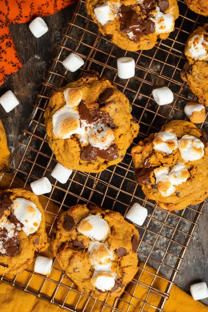 Pumpkin S’mores Cookies cooling on rack with chocolate and marshmallows