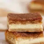 Simple Churro Cheesecake – Easy & Delicious 6 Stacked simple churro cheesecake bars with cinnamon sugar topping and creamy filling on a wooden surface.