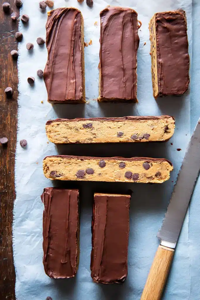 No bake cookie dough bars with chocolate topping and wooden knife on white surface