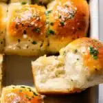 Garlic Butter Bread Rolls (Soft, Fluffy & Flavor-Packed) 15 Freshly baked garlic butter bread rolls with golden crust, parsley, and flaky salt, one roll pulled apart showing fluffy interior