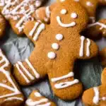 Soft Gingerbread Cookies decorated with white icing in festive shapes like gingerbread men, stars, and trees on a holiday baking surface.