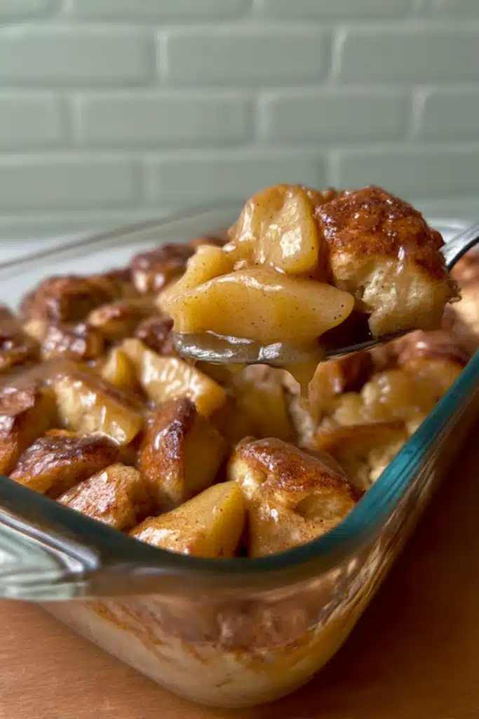 Spoon lifting warm apple pie bubble up from glass baking dish