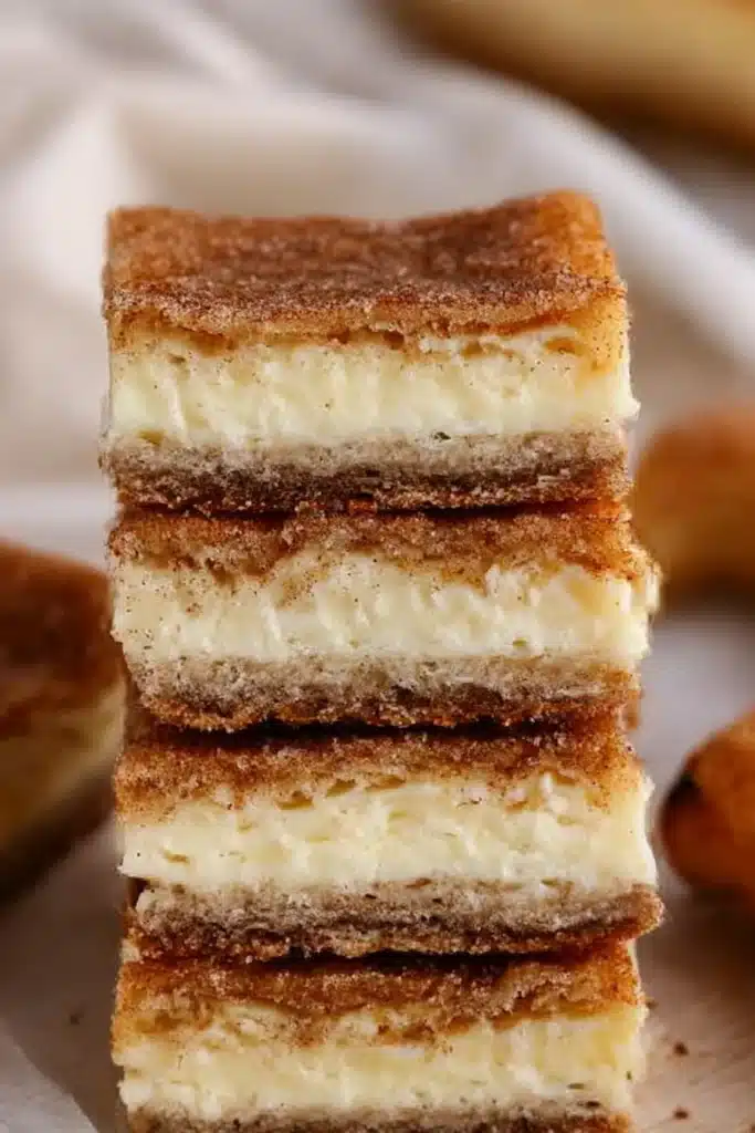 Stacked simple churro cheesecake bars with golden cinnamon crust and creamy layers on a wooden surface.