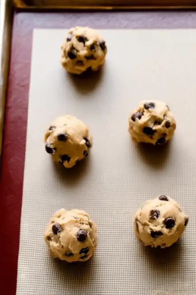Chewy Chocolate Chip Cookies | Soft, Thick & Delicious 16 Tall chocolate chip cookie dough balls spaced on a silicone baking mat