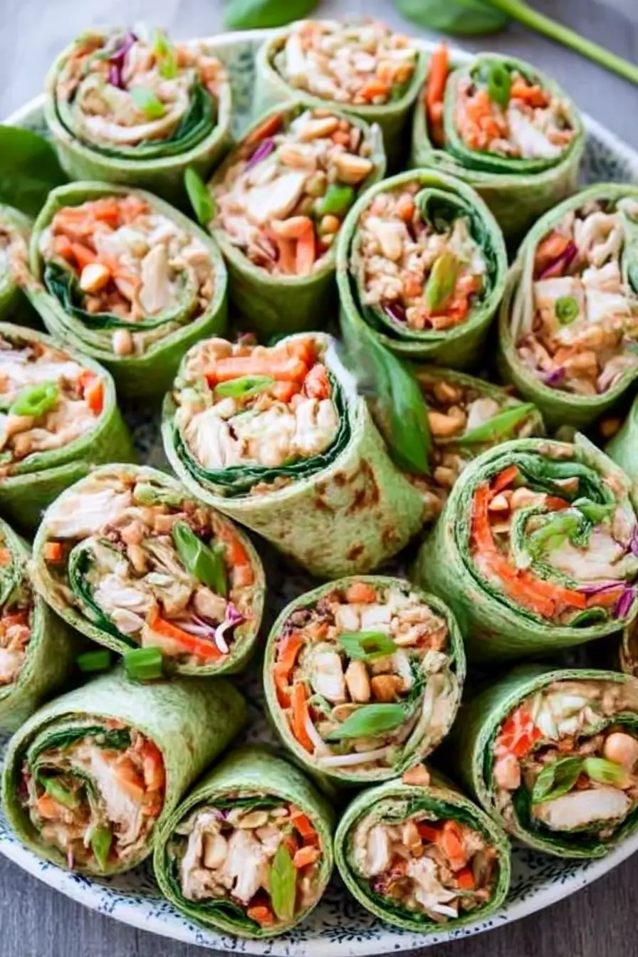 Thai Peanut Chicken Wraps arranged on a platter with spinach and flour tortillas, colorful vegetables, chopped peanuts, and sliced green onions.