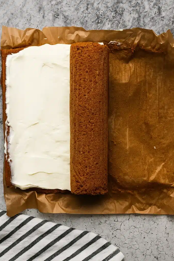 Pumpkin spice roll cake being filled and rolled on parchment paper
