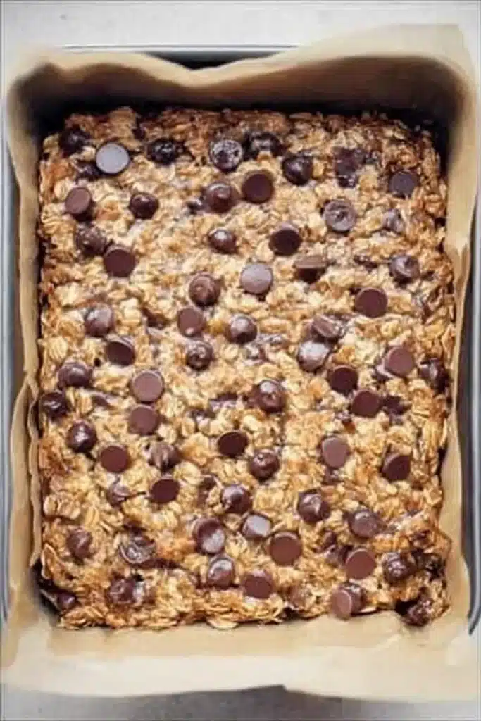 Banana Oatmeal Bars | Quick, Easy & Wholesome Snack 9 Baked banana oatmeal bars with chocolate chips in parchment-lined pan
