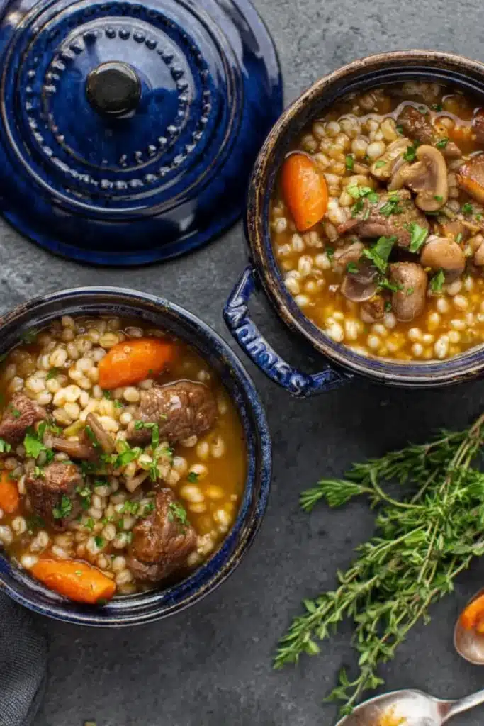 Two small bowls of beef barley soup with carrots, mushrooms, and herbs