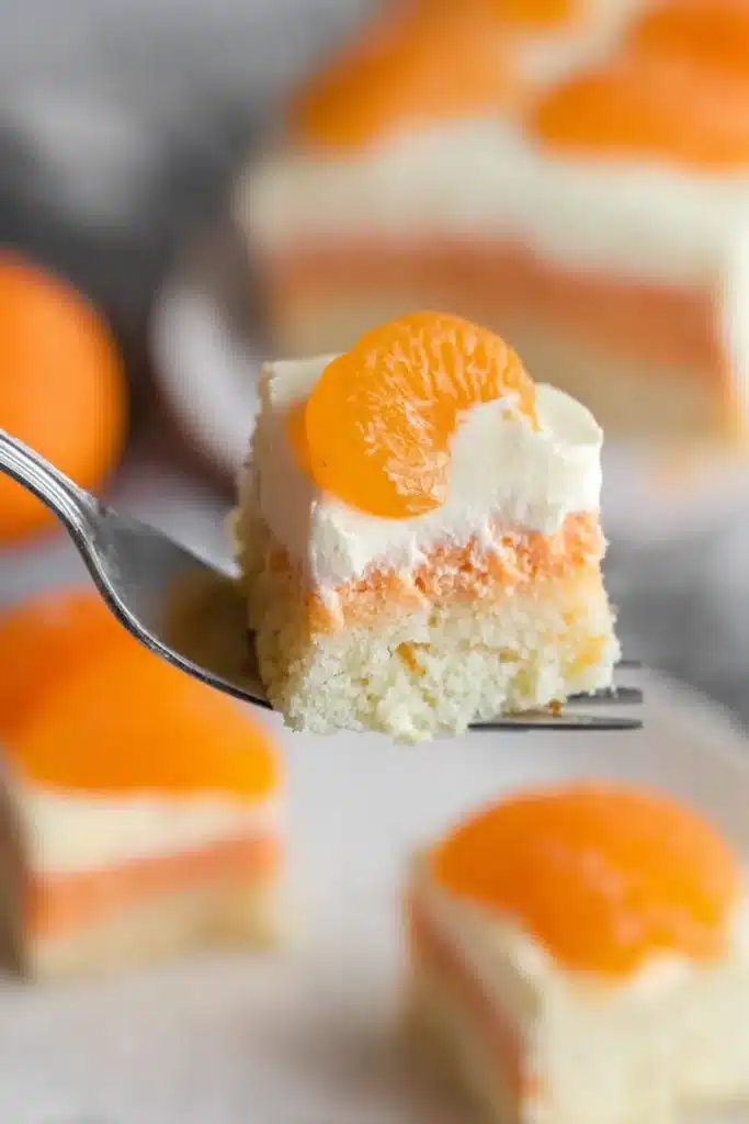 Fork holding a bite of orange creamsicle cake with creamy topping