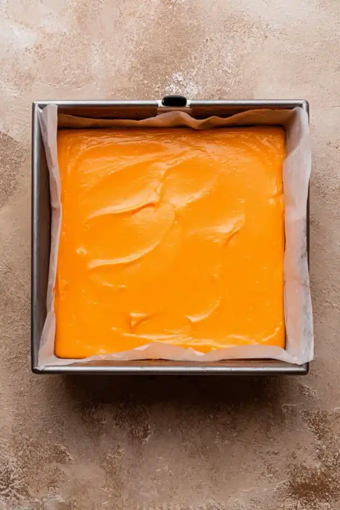 Orange cheesecake layer spread in pan for Halloween brownies