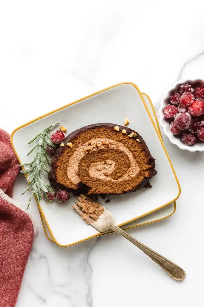 Classic Chocolate Yule Log slice on a gold-trimmed plate with sugared cranberries