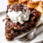 Slice of dark chocolate pecan pie with whipped cream and chocolate curls on a plate