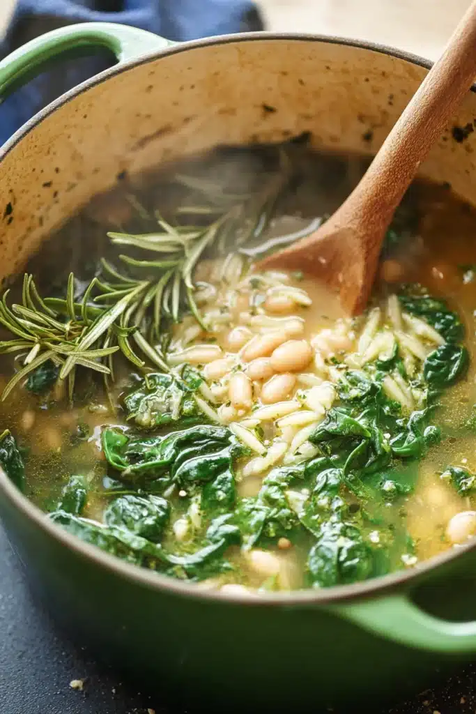 Spinach and white bean soup simmering in Dutch oven with orzo and greens