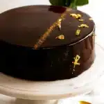 Chocolate mirror glaze cake with gold leaf on marble stand