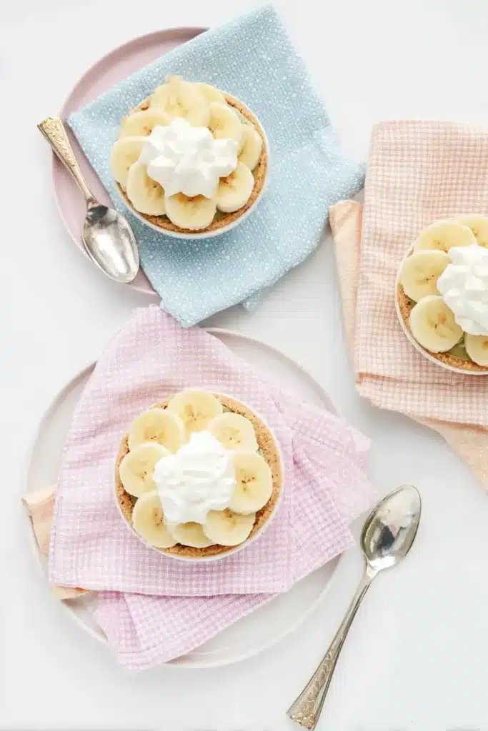 Mini Banana Cream Pies – Quick, Creamy & Delicious 13 Mini Banana Cream Pies on pastel plates with whipped cream and banana slices