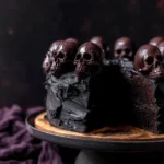 Halloween Chocolate Cake Recipe – Spooky & Delicious Treat 20 Sliced Halloween chocolate cake with black frosting and chocolate skulls on a dark cake stand
