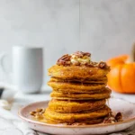 Stack of healthy pumpkin pancakes with maple syrup and pecans
