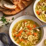 Bowl of lemon chicken orzo soup with carrots, chicken, and bread