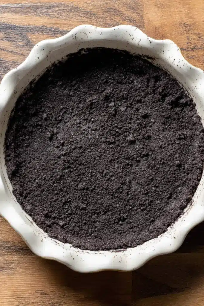 Unbaked Oreo cookie crust in pie dish on wooden surface