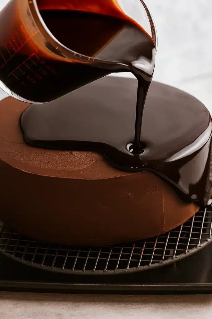 Pouring chocolate mirror glaze onto a frosted cake