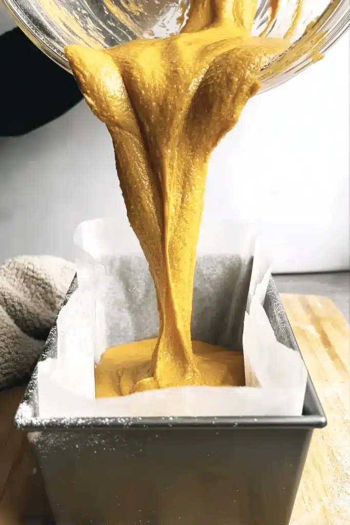 Pouring rich pumpkin bread batter into a parchment-lined loaf pan