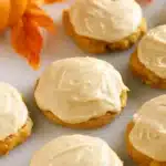 Soft pumpkin cookies with caramel frosting on a fall-themed surface