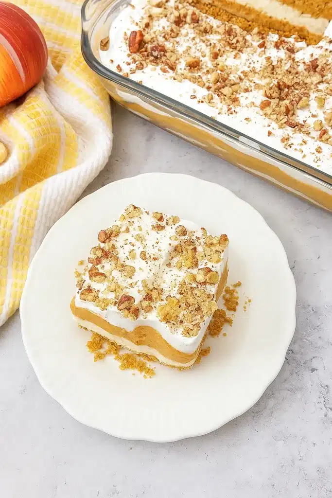 Pumpkin lush dessert slice with whipped topping and pecans on a white plate