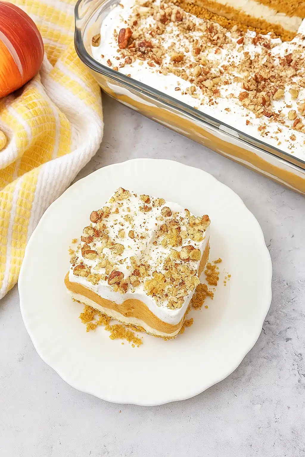 Pumpkin lush dessert slice with whipped topping and pecans on a white plate