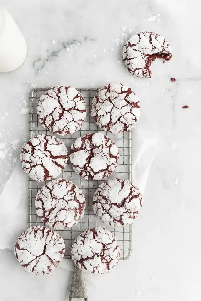 Overhead view of red velvet crinkle cookies on cooling rack with a bitten cookie nearby