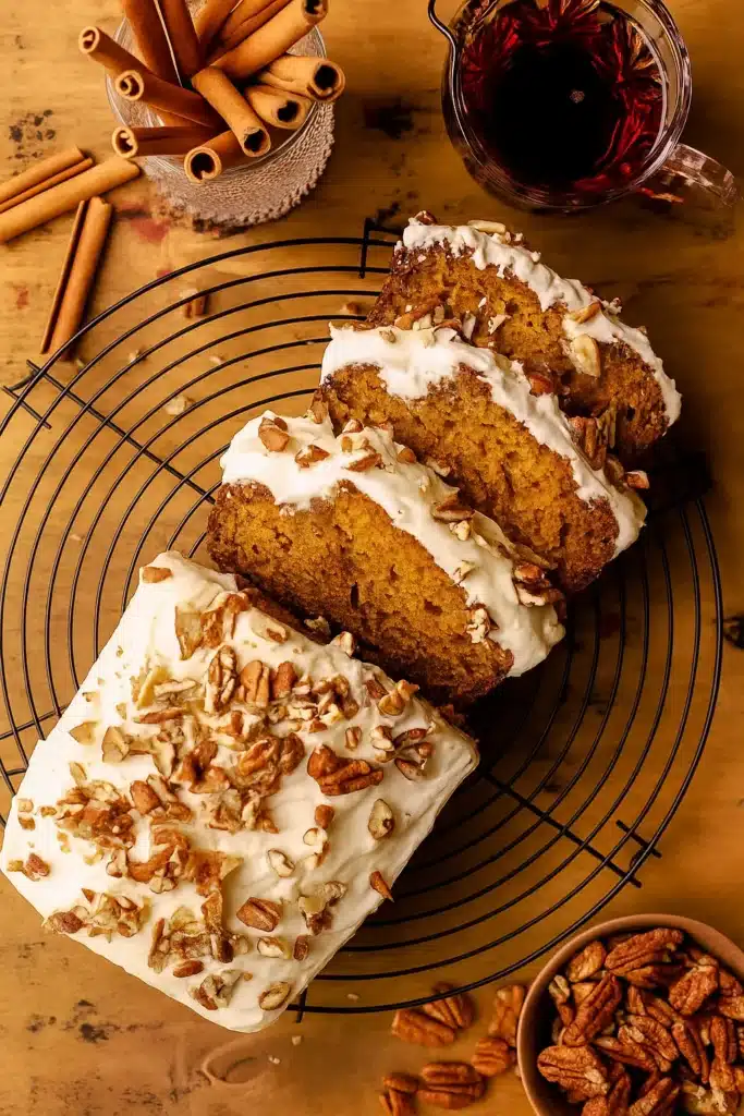 Frosted pumpkin bread sliced on cooling rack with pecans and cinnamon