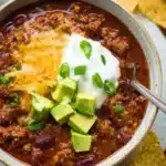 Bowl of slow cooker chili with avocado, sour cream, cheese, and tortilla chips