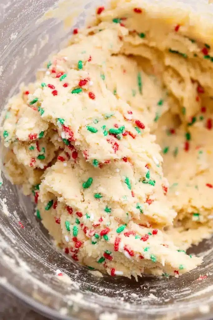 Sugar cookie cheesecake dough with red and green holiday sprinkles in a mixing bowl