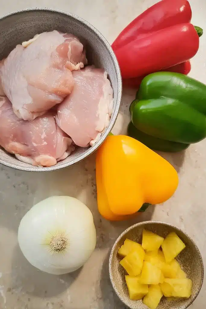 Raw ingredients for sweet and sour chicken with peppers, onion, pineapple, and chicken thighs