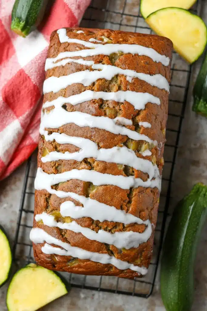 Pineapple Zucchini Bread | Moist & Easy Summer Recipe 5 Whole glazed pineapple zucchini bread loaf on a cooling rack with fresh ingredients