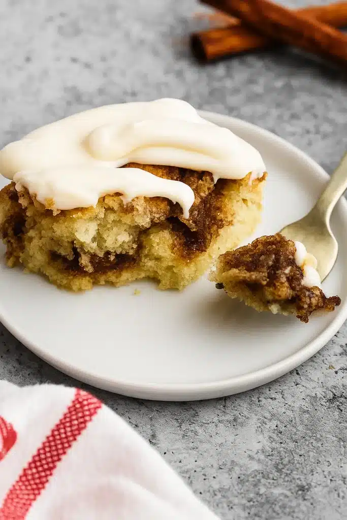 Slice of cinnamon roll cake with cream cheese frosting and a bite on fork