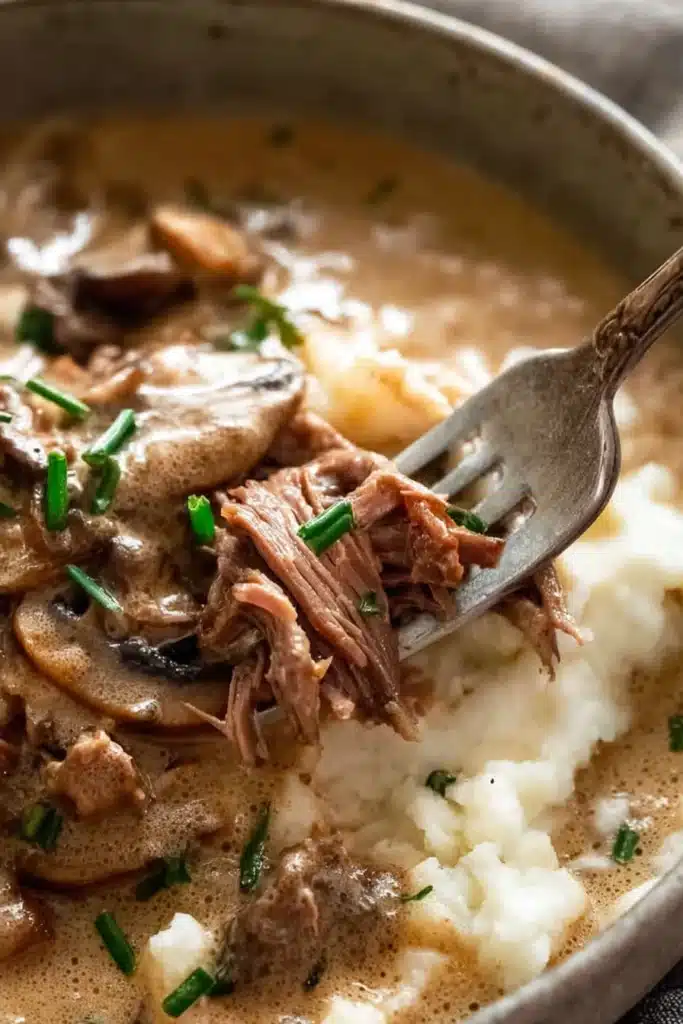 Fork shredding tender beef stroganoff in creamy mushroom sauce