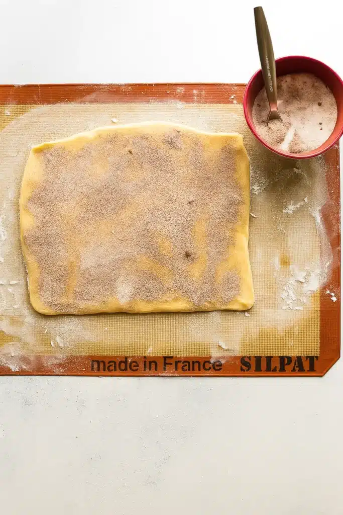 Cinnamon sugar filling spread over cookie dough on silicone baking mat