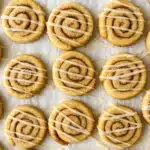 Cinnamon roll cookies with vanilla icing drizzle on baking sheet