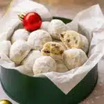 Cranberry orange snowball cookies in a green Christmas tin with powdered sugar