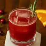 Cranberry orange whiskey sour cocktail with rosemary and ice on wooden table