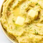 Crockpot mashed potatoes with melted butter and parsley in a white bowl