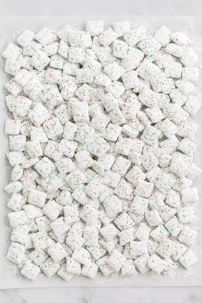 Holiday Puppy Chow Recipe | Easy, Festive & Addictive Snack 10 Holiday Puppy Chow cooling on parchment paper with red and green sprinkles